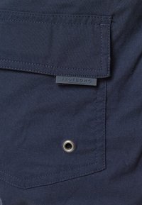 Marinfärgad skjorta i tyg med bröstficka, prydd med en etikett "PROFUOMO," och en metallöggla vid fickans kant.