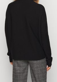 Svart stickad tröja med en något oversized passform, med långa ärmar och en detalj på sömmen bak. Matchad med grå rutiga byxor.