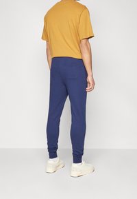 Žluté tričko s krátkým rukávem v kombinaci s přiléhavými tmavě modrými tepláky, které mají zadní kapsu a žebrované manžety. Celý outfit doplňují bílé tenisky.