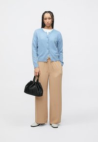 Ανοιχτό μπλε ζακετάκι, μπεζ παντελόνι με ψηλή μέση, μαύρη τσάντα με πτυχώσεις και λευκά παπούτσια. Λείο ύφασμα, άνετη εφαρμογή και κούμπωμα με κουμπιά.