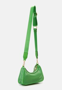 Svetle zelená síťová taška přes rameno se zlatými detaily a nastavitelným širokým popruhem visící na bílém pozadí.
