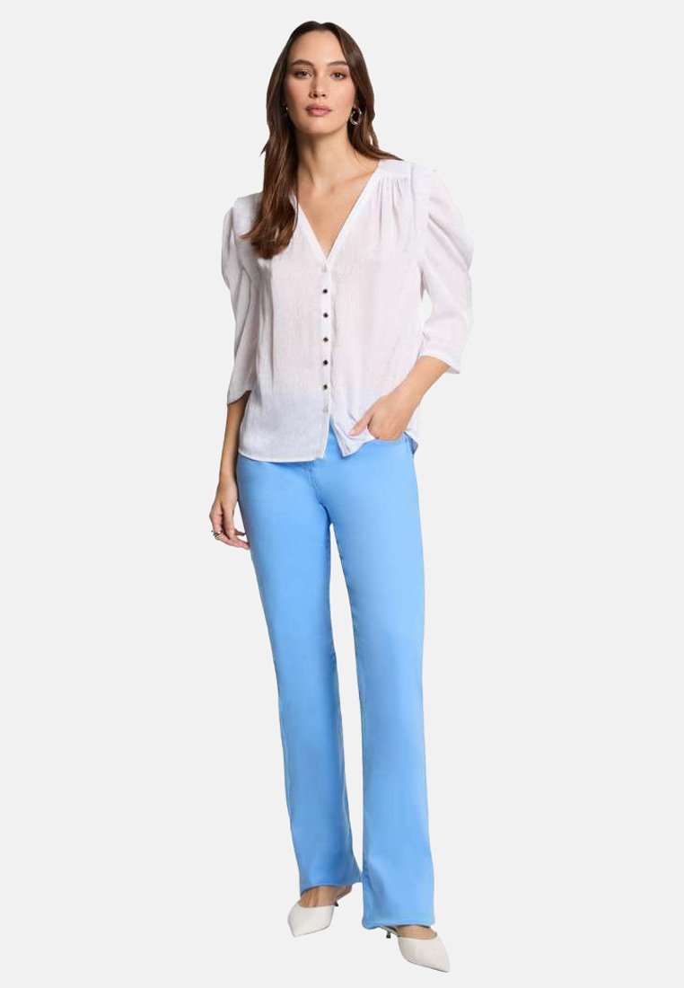 Camicia bianca a maniche a sbuffo, abbinata a pantaloni a palazzo azzurro chiaro. I pantaloni hanno una texture liscia e una vestibilità su misura.