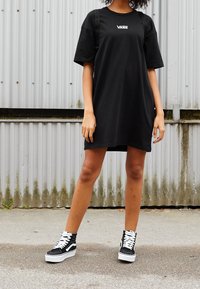 Czarna, oversize sukienka t-shirt z logo Vans, w połączeniu z czarno-białymi, wysokimi trampkami z białymi sznurowadłami i teksturowanym materiałem.