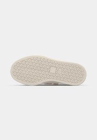 Semelle d'une chaussure beige avec un motif hexagonal et deux petits logos rectangulaires près du centre pour l'adhérence et le marquage.