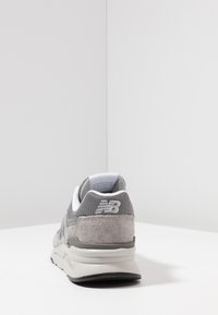 Tenis gri din materiale din suede și plasă, având o talpă căptușită, formă rotundă și accente albe. Vedere din spate care afișează logo-ul brandului.