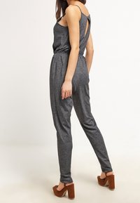 Mono gris carbón con cintura ajustada, detalle de espalda descubierta y piernas ajustadas. Combinado con zapatos de tacón altos marrones.