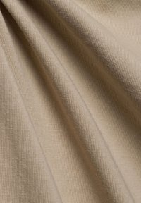 Light beige fabric with a textured, ribbed pattern. The material appears soft and slightly stretchy, showing subtle folds and drapes.