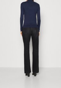 Maglione a collo alto di colore navy abbinato a jeans bootcut neri, con una texture liscia, design aderente e dettagli discreti sulle tasche posteriori.