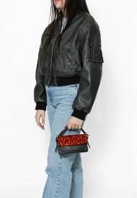 Giubbotto bomber in pelle nera, jeans azzurri chiari e una piccola borsa con base nera e parte superiore in stampa leopardata arancione.