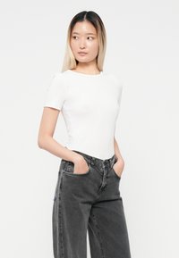 Hvit tettsittende t-skjorte med rund hals, kombinert med høy midje mørk grå denimbukser. Stoffet virker mykt og strukturert.