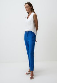 Witte linnen mouwloze top met diepe V-hals, gecombineerd met felblauwe linnen broek met een elastische trekband in de taille en zijzakken.