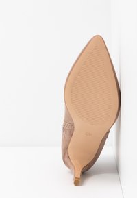 Chaussure à talon haut en daim marron avec un bout pointu. La semelle est beige avec des stries et comporte un indicateur de taille "38". Texture lisse.