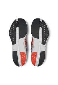 Shoe soles feature a textured black rubber surface with colorful accents in red and white, designed for traction and stability.