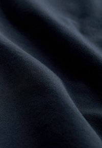 Ciemnoniebieska tkanina o gładkiej fakturze, delikatnie złożona, aby odsłonić subtelne wariacje w odcieniu i głębokości, podkreślające bogactwo materiału.
