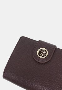 Portafoglio in pelle di un intenso colore viola scuro, caratterizzato da una finitura testurizzata, un dettaglio in metallo circolare dorato e una chiusura a patta. Forma rettangolare compatta.