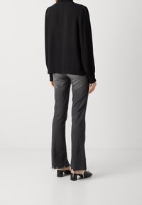 Blusa nera plissé con maniche lunghe, abbinata a jeans grigi scuri a campana con orlo grezzo e sandali neri con tacco quadrato.
