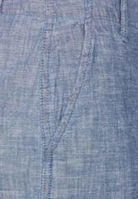 Tessuto di lino azzurro chiaro con una texture morbida, caratterizzato da tasche angolate e dettagli di cucitura a contrasto.