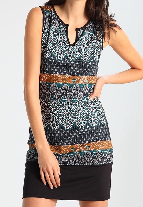 Femme portant une robe sans manches à motifs géométriques et floraux en noir, blanc, sarcelle et marron, debout avec une main sur la hanche.