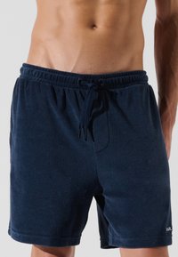Tmavomodré šortky z froté látky s elastickým pásom, nastaviteľnou šnúrkou a bočnými vreckami. Obsahujú malé logo na leme.