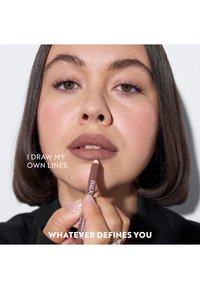 Nahaufnahme einer Person, die einen nudefarbenen Lippenkonturenstift auf ihre Lippen aufträgt. Glatte Haut, mittlerer Kontrast in der Beleuchtung und ein weißer Hintergrund.