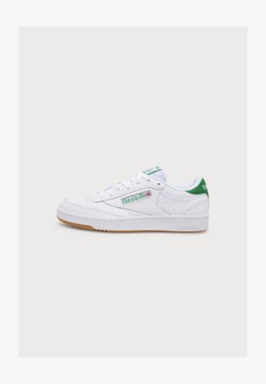 Biela Reebok teniska so zelenými detailmi, gumovou podrážkou, šnúrkami a bočným logom, zobrazená zľava na jednoduchom pozadí.