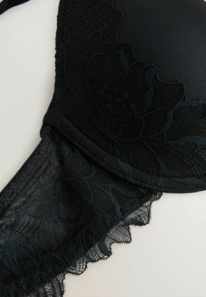 Soutien-gorge en dentelle noire doté de motifs floraux, de bonnets lisses, de bretelles réglables et de bords festonnés, mettant en valeur une texture et un design raffinés.