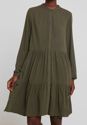 Długa sukienka na długi rękaw w oliwkowym kolorze, z wielowarstwowymi falbanami, okrągłym dekoltem i ukrytymi guzikami z przodu, noszona przez osobę na jednolitym tle.