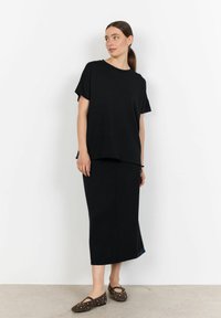 Černý top s krátkým rukávem a odpovídající midi sukně vyrobené z měkké látky. Tento outfit má volný střih a jemné boční rozparky. Hnědé ploché boty se cvočky.