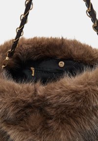 Brun faux fur tote taske med et sort stofinteriør, der har en lynlås lomme og guldfarvede hardware detaljer. Flettet strop integreret med kædeled.