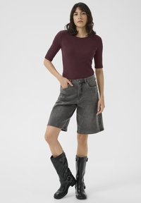 Burgundy ribbed short-sleeve top paired with high-waisted gray denim shorts. Black knee-high boots with buckles and a smooth finish.