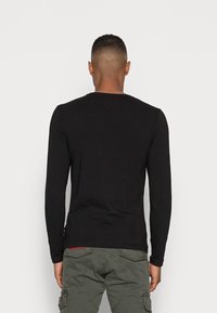 Schwarzes langärmliges Shirt aus Baumwolle mit rundem Halsausschnitt und taillierter Passform, getragen mit grünen Cargo-Hosen.