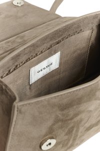 Interior de bolso de ante color canela con un acabado suave, que cuenta con un bolsillo y una etiqueta con la marca "GESTUZ". Los cierres incluyen un botón de presión plateado.