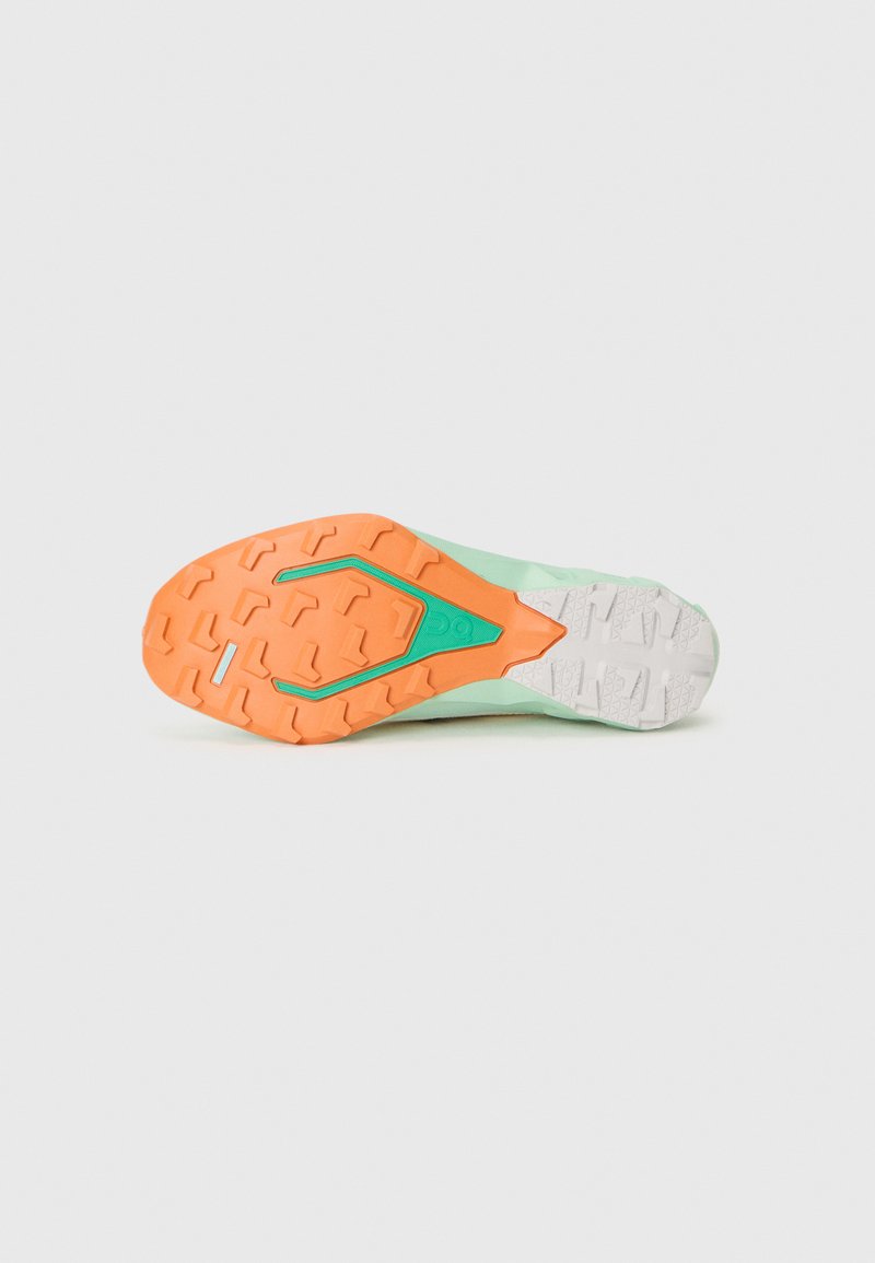 Suela de zapatilla de trail running, con un agarre de goma naranja, un talón blanco y una sección superior de color verde claro con patrones texturizados.