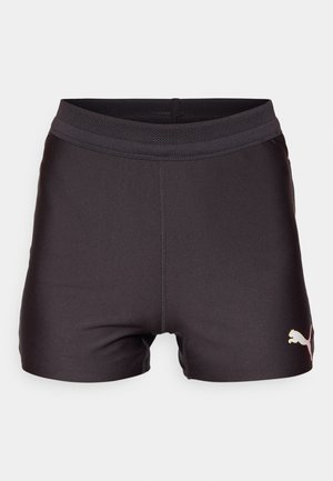 Svart treningshorts med et glatt, elastisk stoff, med en mesh-linning og en gull Puma-logo nederst til venstre.