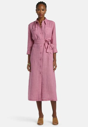 Moteris vilki rožinės spalvos midi suknelę su mygtukais, 3/4 rankovėmis ir surišta juosmens juosta, derina su smėlio spalvos atvirais bateliais ir auksiniais papuošalais.