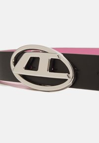 Cinturón de cuero negro con interior rosa, que presenta una hebilla ovalada plateada con un diseño recortado, proporcionando un contraste moderno.