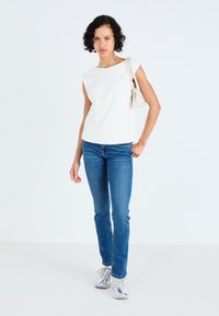 Hvid ærmeløs top, blå jeans og sølvfarvede sneakers. Toppen har en ret snit og en glat tekstur med et minimalistisk design.