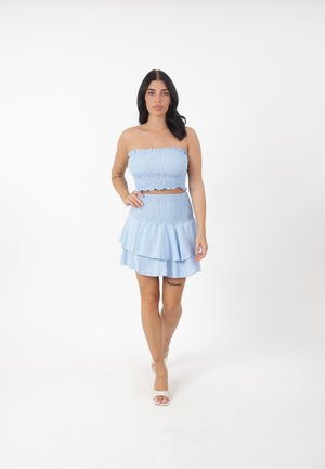 Helles blaues Zweiteiler-Set mit einem gerafften, trägerlosen Crop-Top und einem gestuften Minirock mit fransigen Kanten. Glattes, strukturiertes Material.