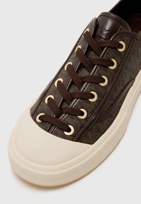 Baskets marron et beige avec des lacets marron foncé, des œillets dorés et un motif texturé, avec le logo MK sur la languette et le bord de la semelle marqué.