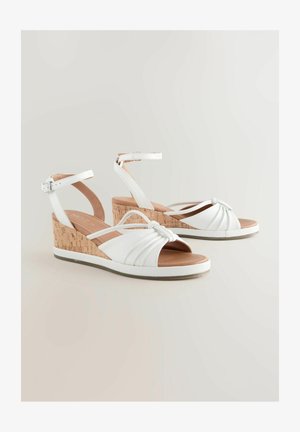Sandales à talons wedges blanches avec un talon en liège, dotées d'un design à l'avant noué, d'une bride réglable à la cheville et d'un dessus en cuir souple texturé.