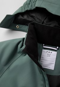 Grøn vandtæt jakke med en sort fleece-krave, elastiske manchetter og et mærke med størrelse og plejeinstrukser indeni.