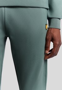 Groene joggingbroek van textuurstof, met een gele geborduurde logo aan de zijkant en een tapered fit met elastische boorden.