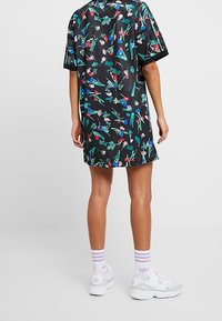Krótka czarna sukienka w kwiatowy wzór o luźnym kroju, wykonana z gładkiego materiału. Posiada krótkie rękawy i okrągły dekolt, zestawiona z białymi trampkami.