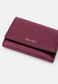 Πορτοφόλι Calvin Klein σε σκούρο μπορντό δέρμα με υφή, που διαθέτει αναδιπλούμενο σχέδιο και ασημένια λεπτομέρεια λογότυπου μπροστά.