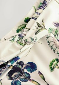 Blütenmusterstoff in Creme mit grünen und lila botanischen Designs. Weiche Textur mit einem geknoteten Detail in der Mitte.