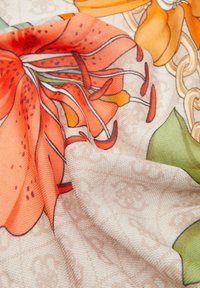 Sciarpa floreale con grandi gigli arancioni e foglie verdi su uno sfondo beige chiaro con motivi intricati, realizzata in tessuto morbido e testurizzato.