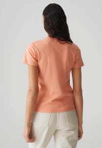 T-shirt aderente a maniche corte di colore corallo, realizzato in morbido cotone. Presenta un collo rotondo e dettagli di cucitura delicati sulle maniche.