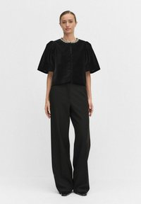 Czarny krótki top z dekoltem w kształcie łódki i pluszową teksturą, w połączeniu z czarnymi spodniami z wysokim stanem i czarnymi płaskimi butami.