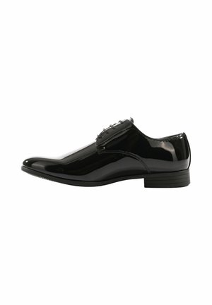 Scarpa elegante da uomo in pelle nera lucida con lacci e tacco basso impilato, mostrata di profilo su sfondo bianco.