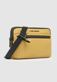 Gelbe und schwarze Umhängetasche mit rechteckiger Form, texturiertem Material, verstellbarem Riemen und einer vorderen Tasche mit Reißverschluss.